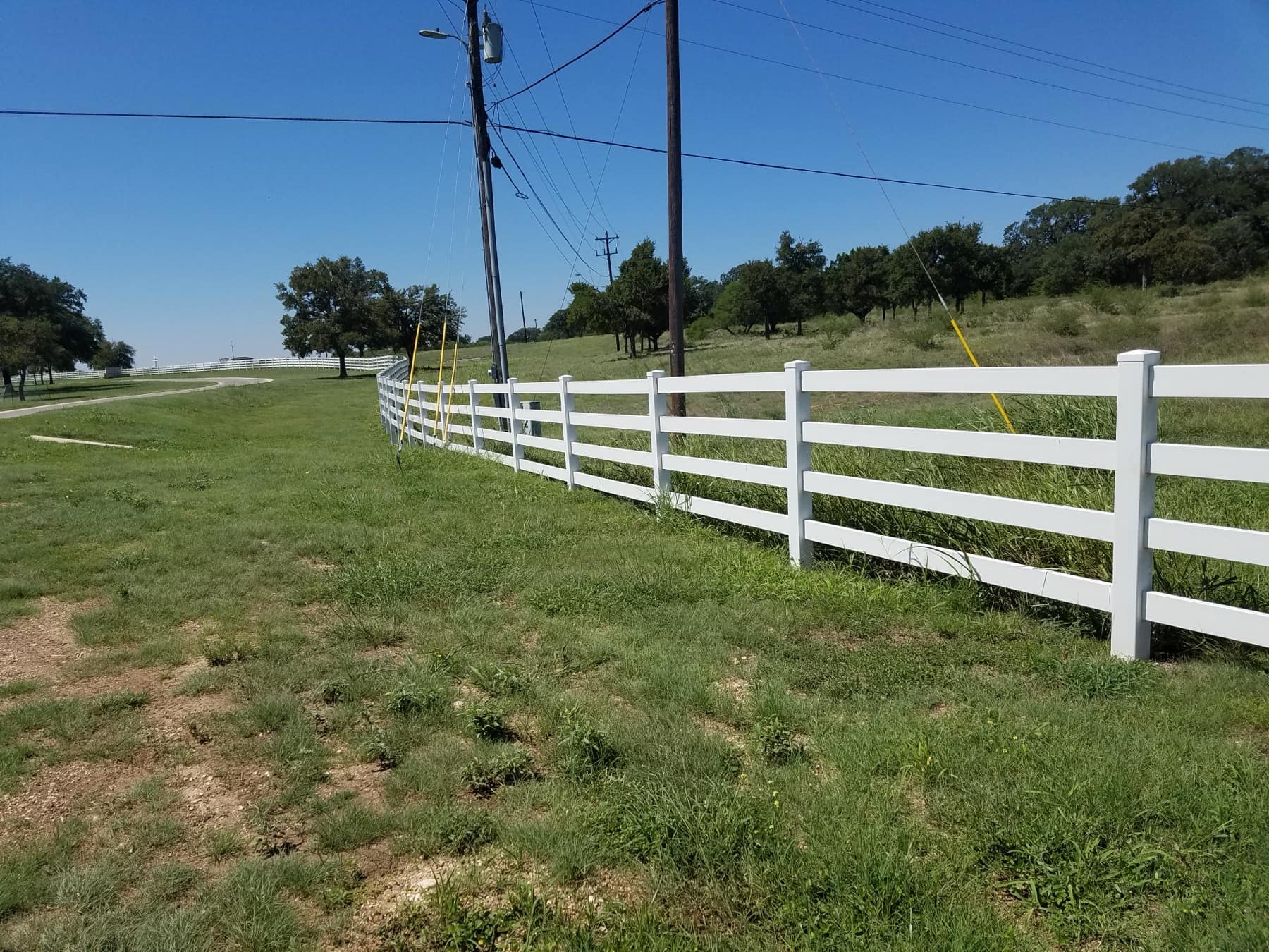 White four-rail ranch fence running across a green pasture