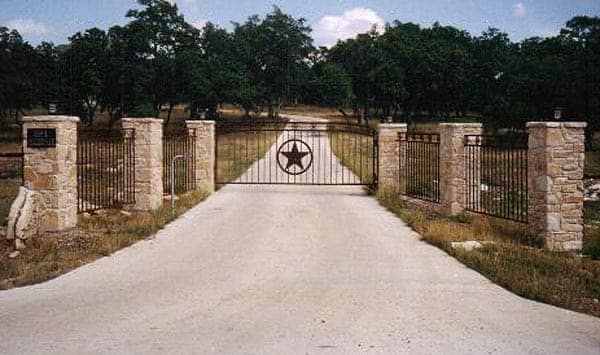 Iron gate with a Texas star between limestone columns across a long drive